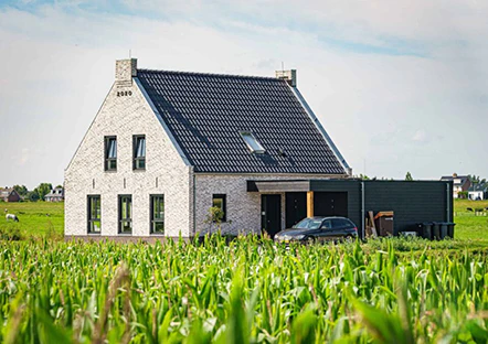 Modern landelijke woning met witte bakstenen, donker dak en strakke zwarte kozijnen, omgeven door een veld met mais. Een zwarte auto staat geparkeerd bij de oprit.