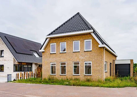 Gezinswoning met gele bakstenen en donker dak. Een moderne, duurzame woning in een rustige buurt. Naastgelegen huis heeft zonnepanelen.