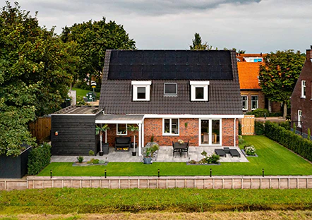 Modern huis met zonnepanelen op het dak, groene tuin met terras en strakke bestrating. Een duurzaam en energiezuinig thuis in een rustige buurt.