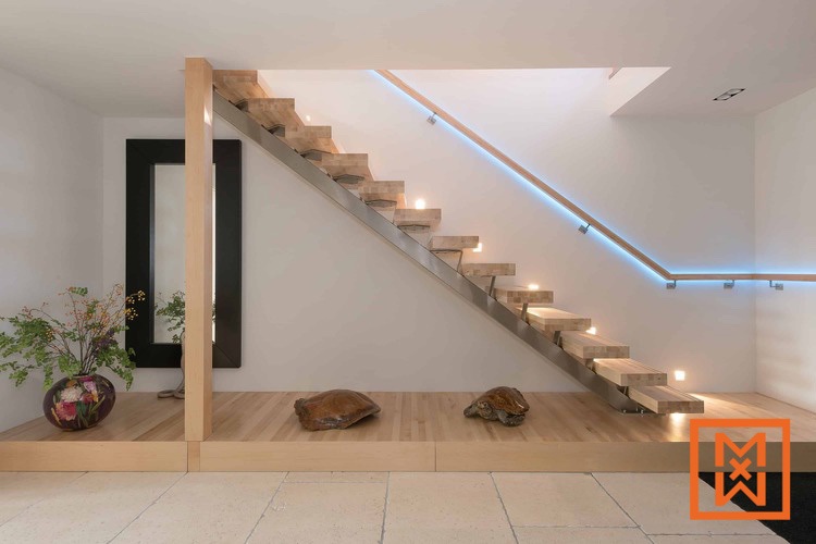 Moderne, minimalistische trap met lichthouten treden en roestvrijstalen leuningen, verlicht door inbouwspots. De trap heeft een strak, eigentijds ontwerp, met twee decoratieve schildpadden op een lichthouten bordes eronder.