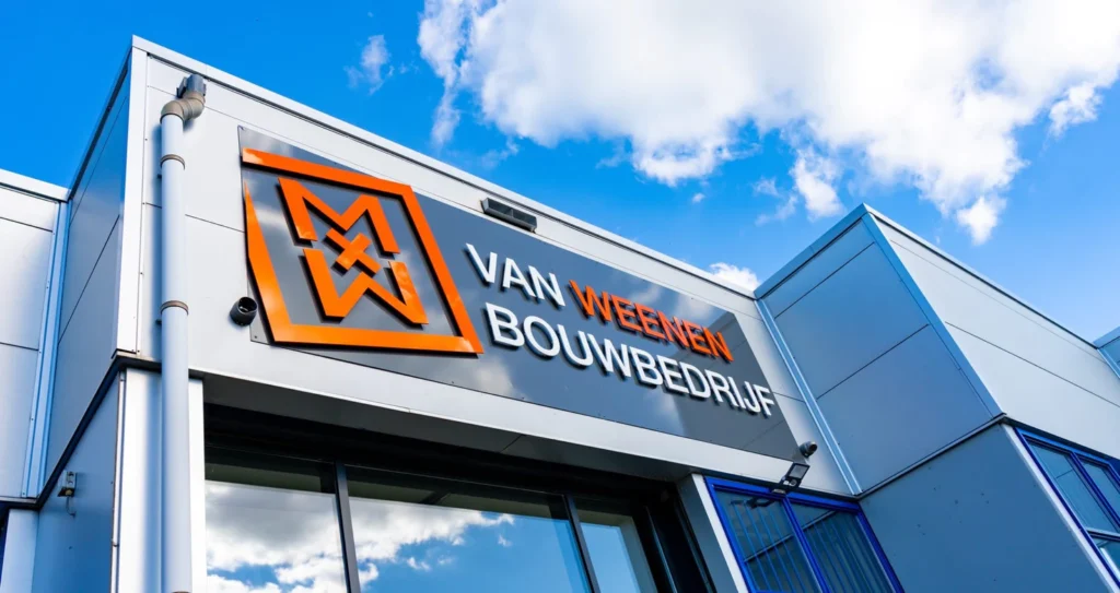 Kantoorgevel van Van Weezen Bouwbedrijf met logo tegen een blauwe lucht. Het logo is oranje en de tekst "Van Weezen Bouwbedrijf" is prominent aanwezig.