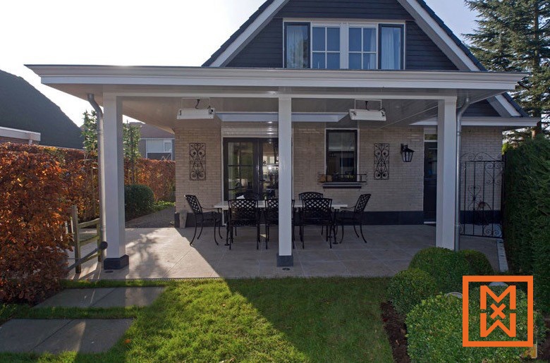 Modern terrasontwerp met een overdekte eethoek met een strakke, witte pergola, zwart metalen tuinmeubilair en een lichtbeige bakstenen huis. De ruimte is elegant aangelegd met verzorgde hagen en een weelderig groen gazon.
