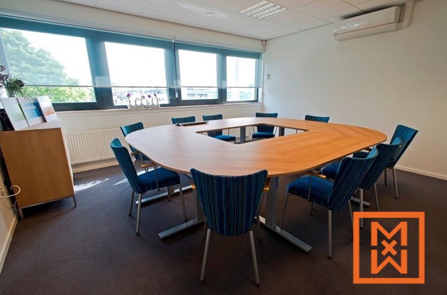 Moderne, U-vormige vergadertafel met teal stoelen in een licht, minimalistisch kantoor. Grote ramen zorgen voor voldoende natuurlijk licht. Ideaal voor zakelijke bijeenkomsten of bedrijfsevenementen.