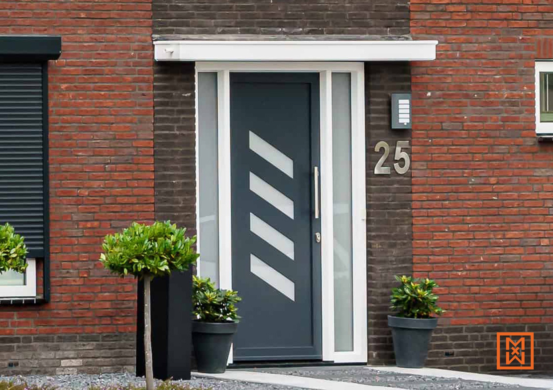 Moderne grijze voordeur met witte accenten en huisnummer 25 in een bakstenen gevel. Potplanten aan beide zijden. Strak design.