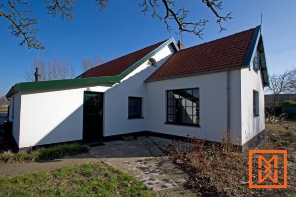 Charmante witte boerderij met een donkergroen dak en accenten, gelegen in een rustige omgeving. De woning heeft donkere kozijnen en een ruim terras. Een strakblauwe lucht zorgt voor een stralende achtergrond.