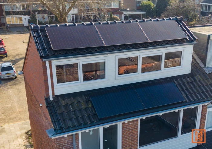 Zonnepanelen op een huis met bakstenen muren en witte kozijnen in een woonwijk.